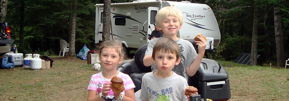 three children with camping trailer in background